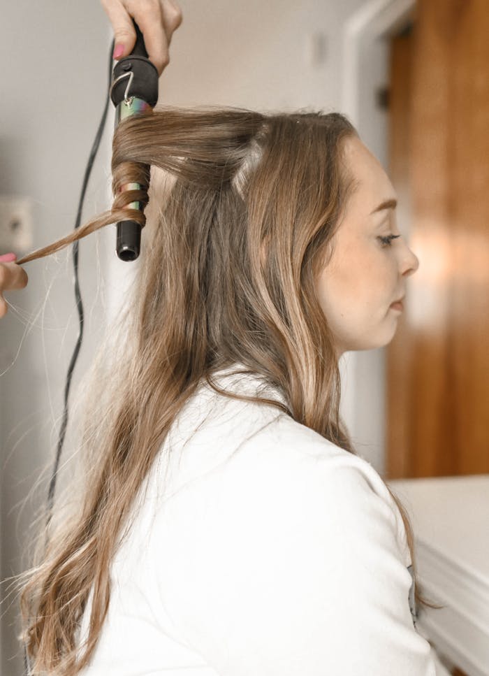 Home Profile of a woman having her hair curled with an iron in a salon setting.